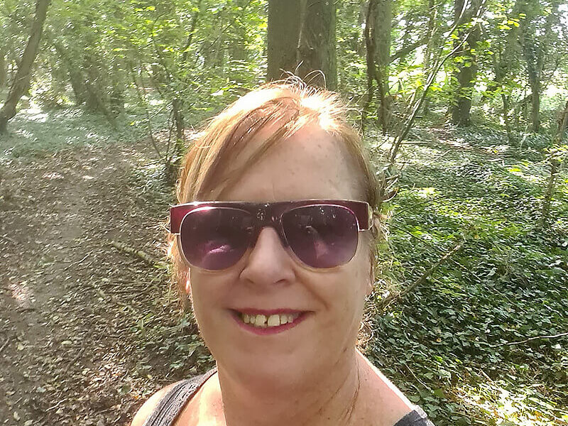 A woman in sunglasses taking a selfie in the woods.