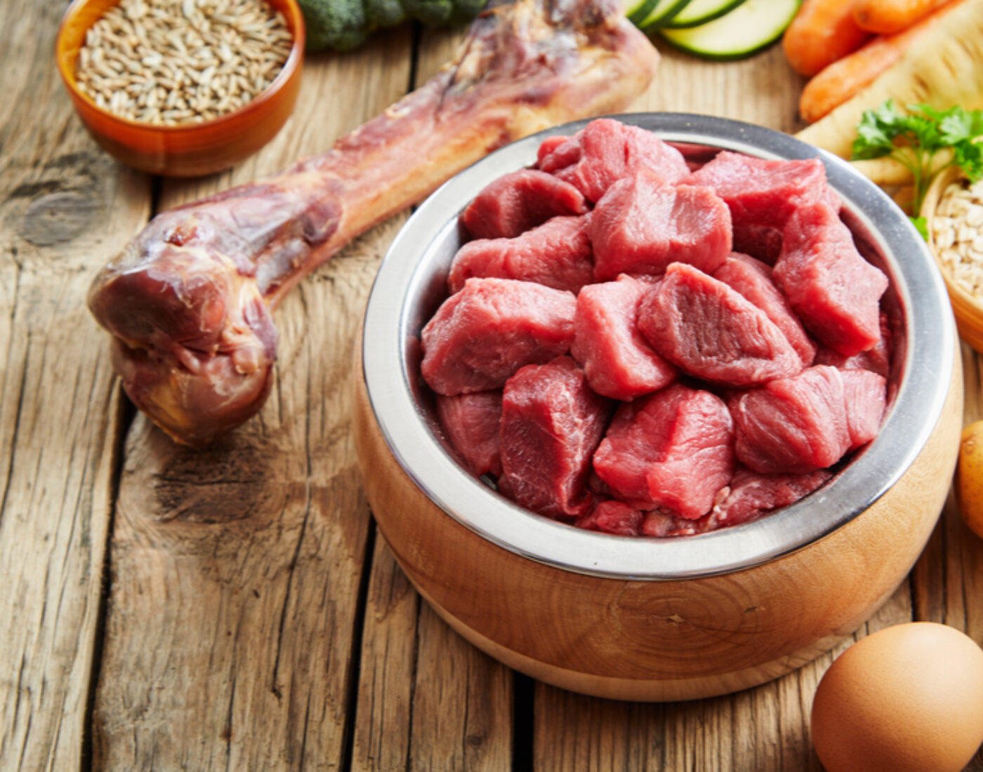 A bowl of meat, vegetables and eggs on a wooden table.